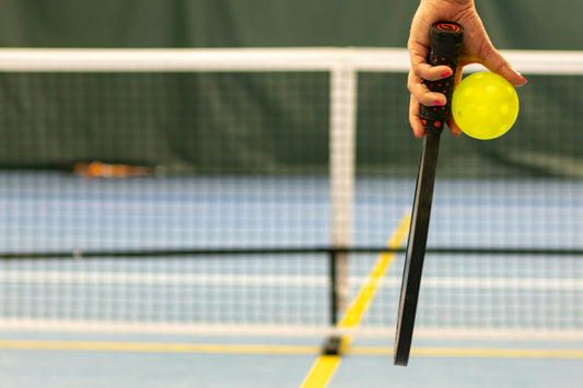 Someone on a pickleball court holding a paddle and ball.